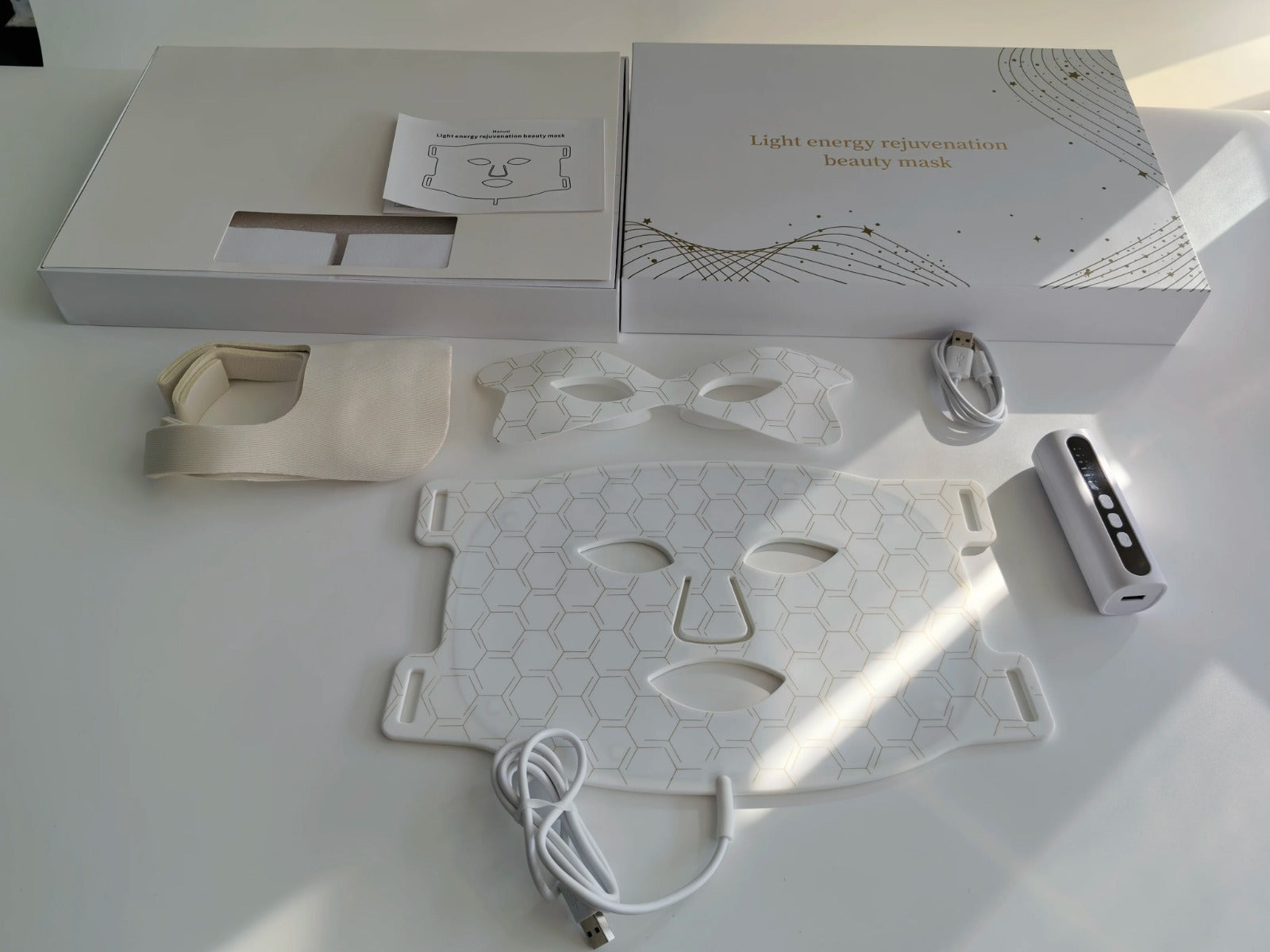 Amporea LED light therapy face mask in white — full kit unboxed: mask, eye mask, controller, USB cable, and gold-detailed packaging